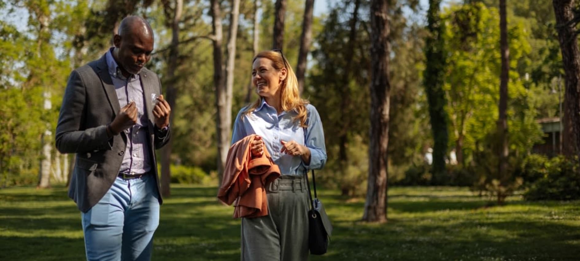 A man and woman walk through a woodland in conversation