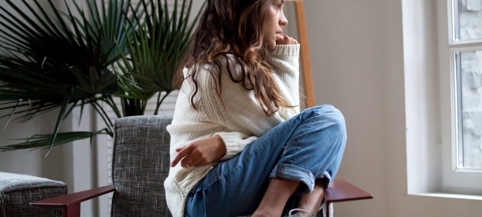 A woman sits on a chair looking out of a window nervously