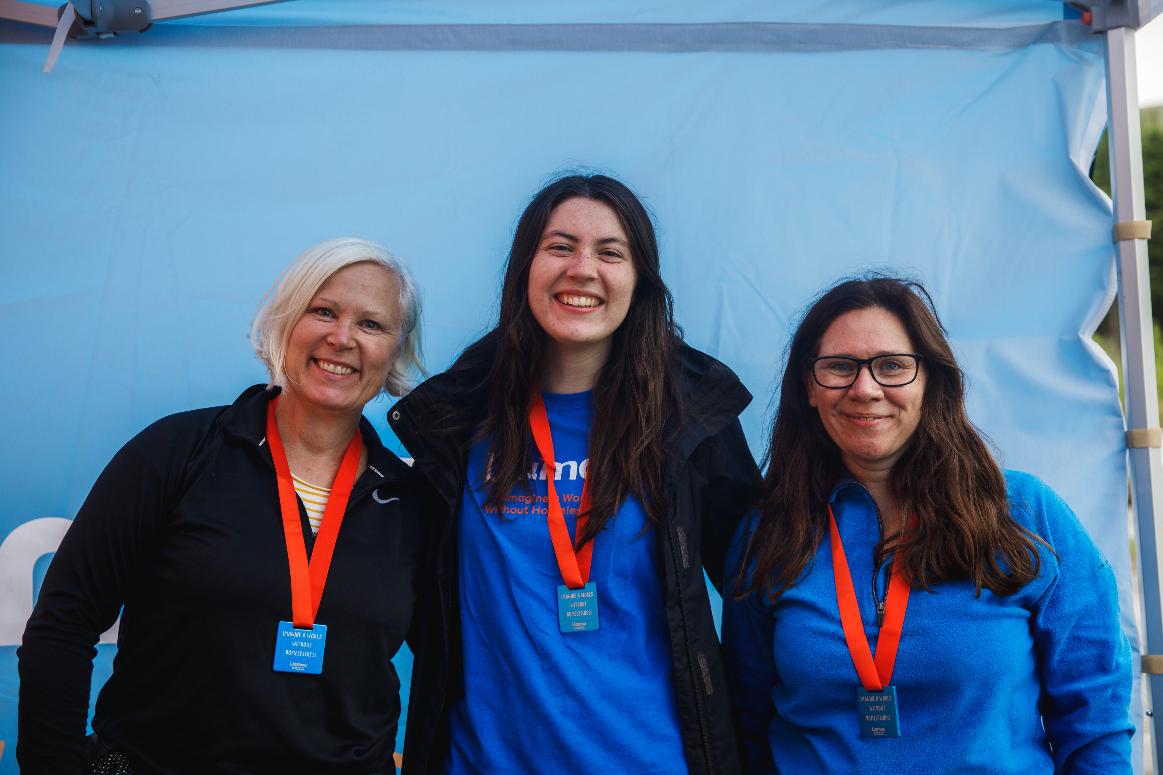 Three women smiling, with the middle woman wearing a Llamau t-shirt.