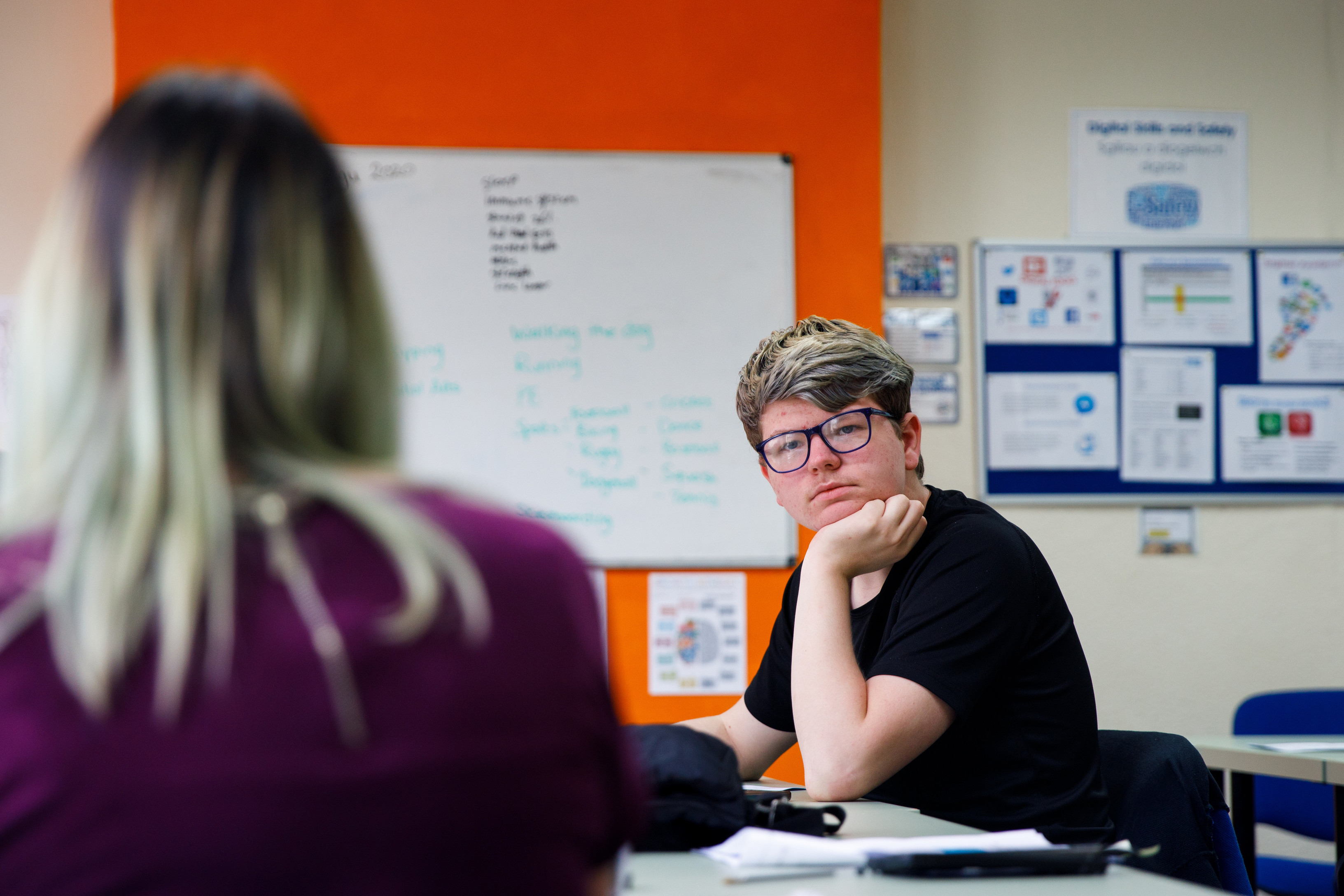 A teenage boy sat in a classroom with his head rested on his hand, listening to the teacher.