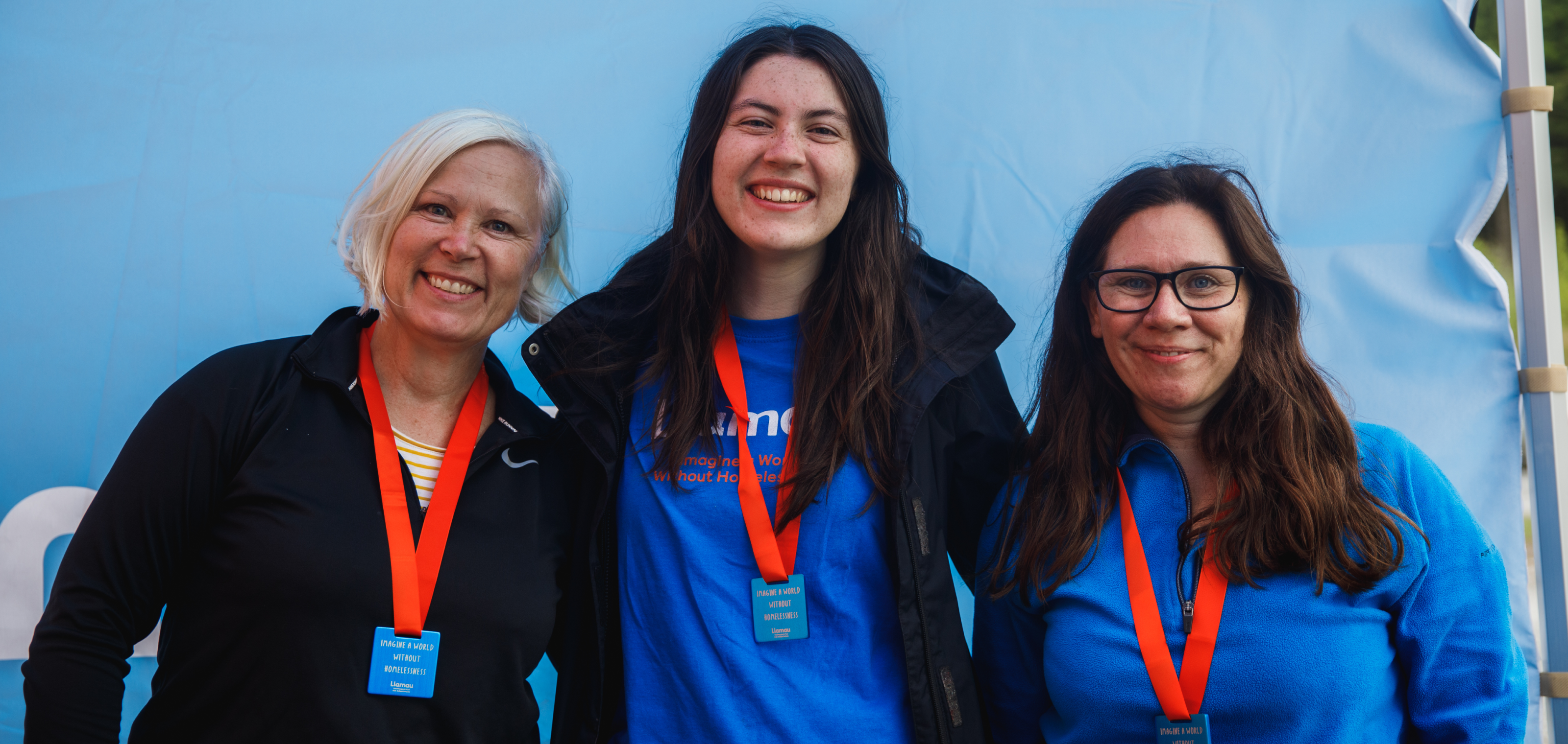 Three female fundraising participants wearing Llamau t-shirts and medals smile for the camera